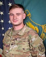 Man in U.S. Army uniform standing in front of two flags.