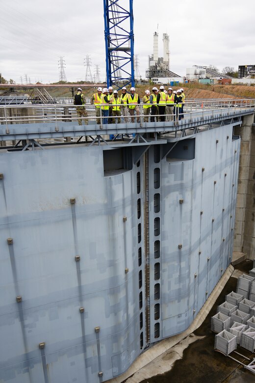 A group of people in vests and hardhats stands on top of miter gates on a navigation lock.