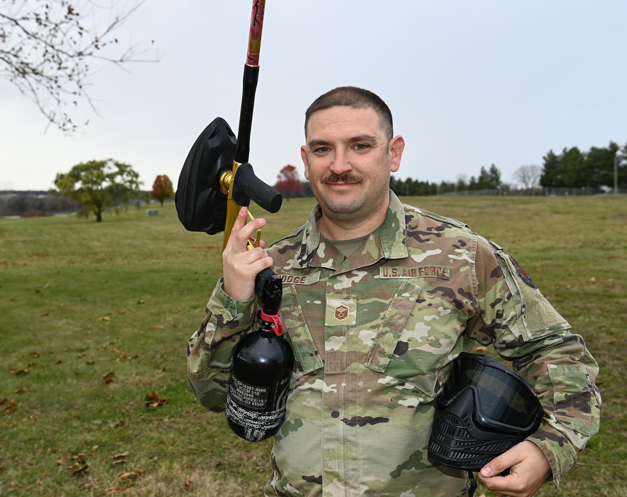 Airman in camo uniform poses outside with paintball gun and mask