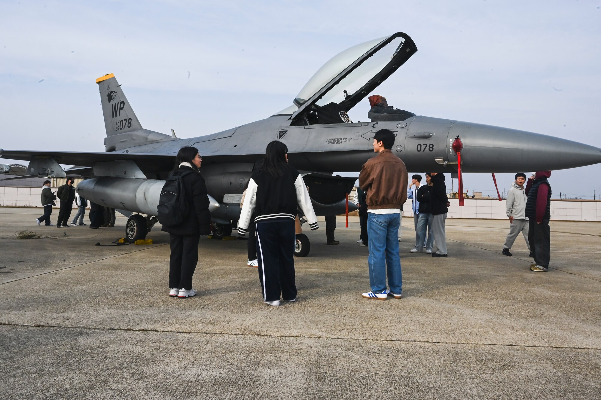 8th Fighter Wing Airmen pose for a photo with students from Kunsan National University in front of a U.S. Air Force F-16 Fighting Falcon aircraft.