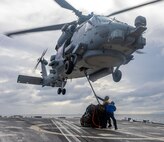 BM2 Riley Etchison connects a sling to the cargo hook of an MH-60R Sea Hawk helicopter from HSM-51, as BMSA Adrien Perges secures him for safety during a vertical replenishment aboard USS Preble (DDG 88) in the north Pacific Ocean.