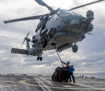 BM2 Riley Etchison connects a sling to the cargo hook of an MH-60R Sea Hawk helicopter from HSM-51, as BMSA Adrien Perges secures him for safety during a vertical replenishment aboard USS Preble (DDG 88) in the north Pacific Ocean.