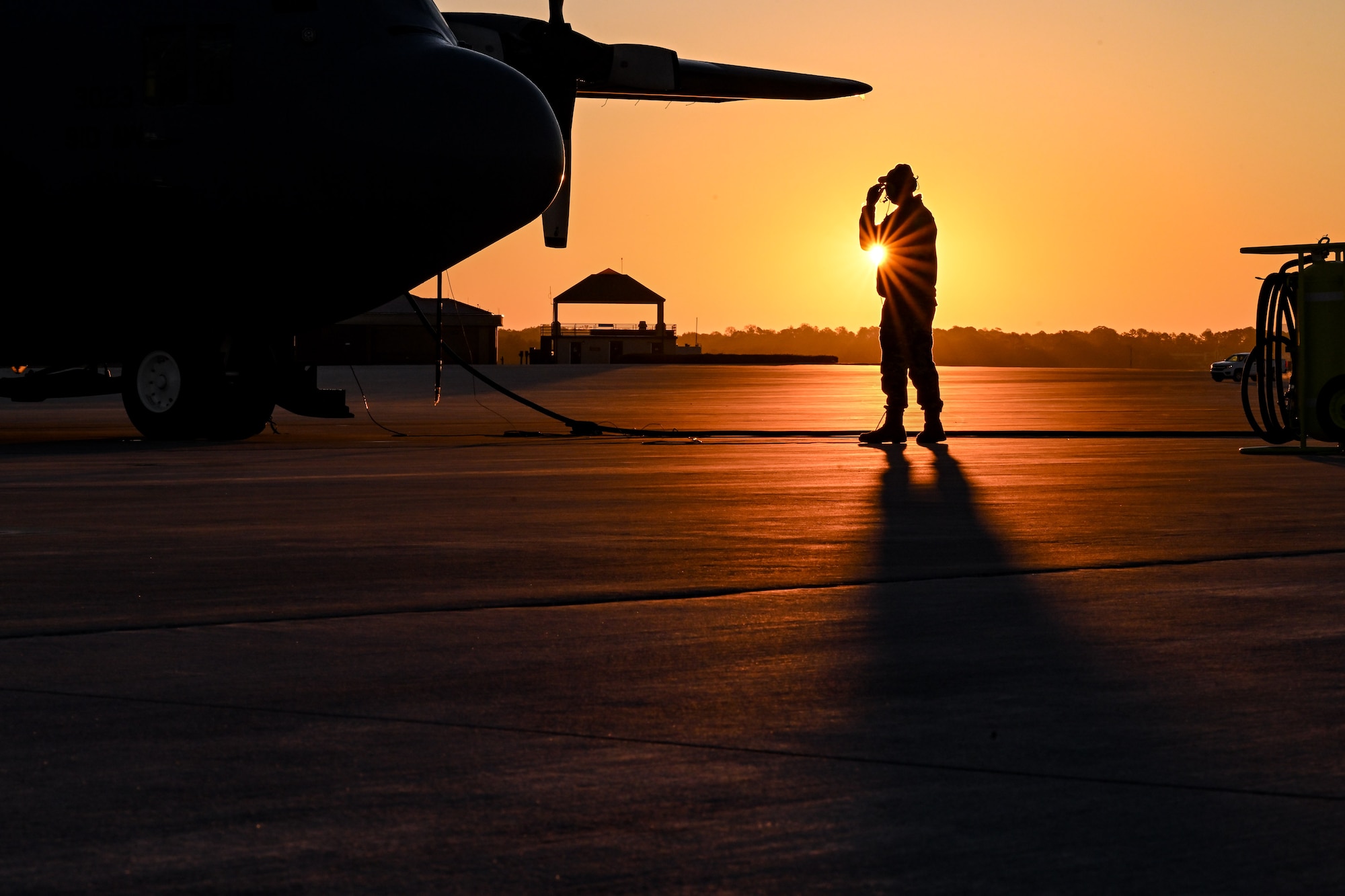 The sun rises behind a Citizen Airman assigned to the 910th Maintenance Squadron on the flightline at Dobbins Air Reserve Base, Georgia, Nov. 16, 2024.