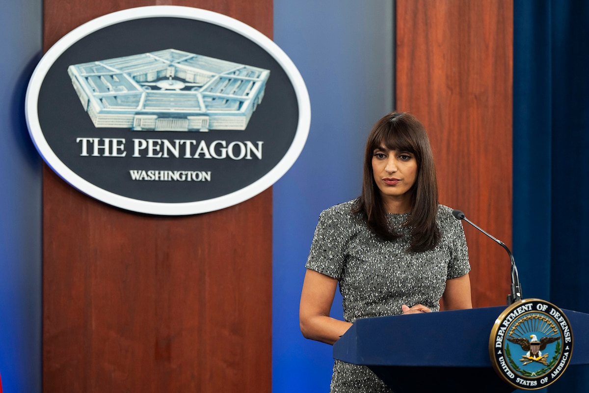 A civilian stands behind a podium with a sign behind them.