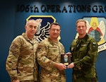 U.S. Air Force Col. Jeffrey Cannet, 106th Rescue Wing commander, and Chief Master Sgt. Edward Rittberg, 106th command chief, receive a plaque from Swedish Lt. Col. Sebastien Blixte, a Swedish Air Force Ranger and chief of operations for Blekinge Wing, Sweden, at Francis S. Gabreski Air National Guard Base, Westhampton Beach, N.Y., Nov. 19, 2024. It was the initial key leader engagement for State Partnership Program partners Sweden and the New York National Guard.