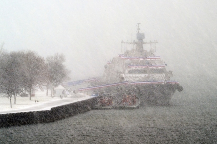 A large ship sits by a dock in a snowstorm.