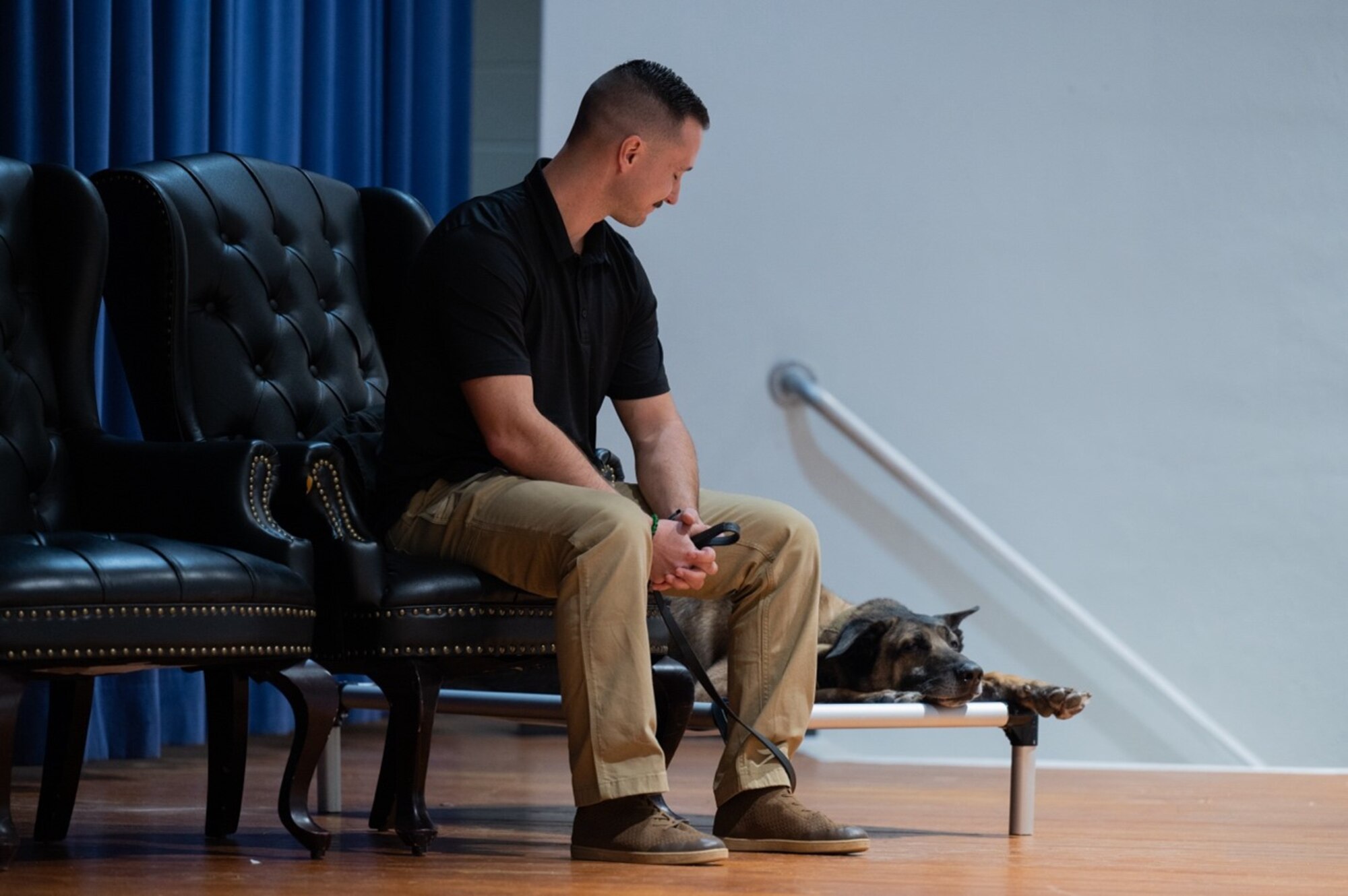 A military working dog and his handler sit on stage during the MWD's retirement.