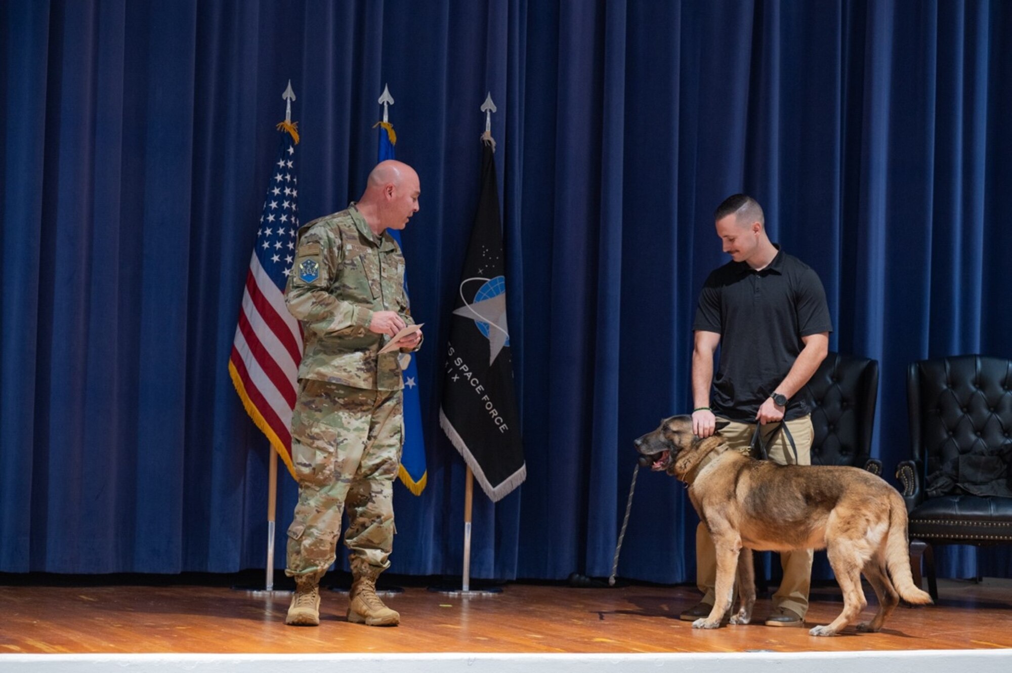 A dog and his handler stand on stage with a military member.