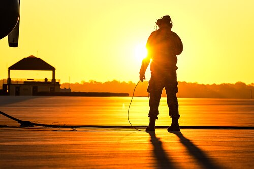 The sun rises behind a Citizen Airman assigned to the 910th Maintenance Squadron on the flightline at Dobbins Air Reserve Base, Georgia, Nov. 16, 2024.