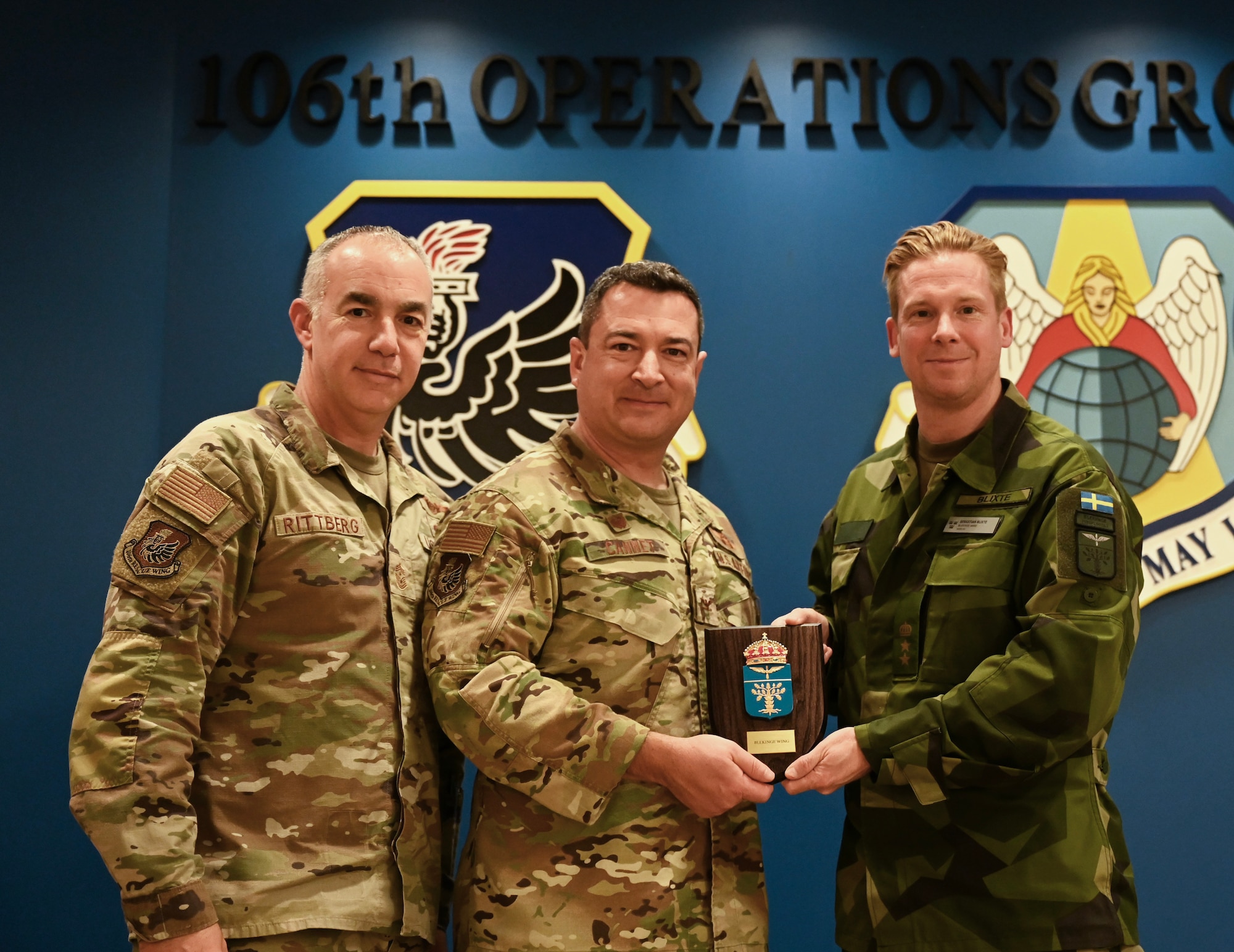 U.S. Air Force Col. Jeffrey Cannet, 106th Rescue Wing commander, and Chief Master Sgt. Edward Rittberg, 106th command chief, receive a plaque from Swedish Lt. Col. Sebastien Blixte, a Swedish Air Force Ranger and chief of operations for Blekinge Wing, Sweden, at Francis S. Gabreski Air National Guard Base, Westhampton Beach, N.Y., Nov. 19, 2024. It was the initial key leader engagement for State Partnership Program partners Sweden and the New York National Guard.