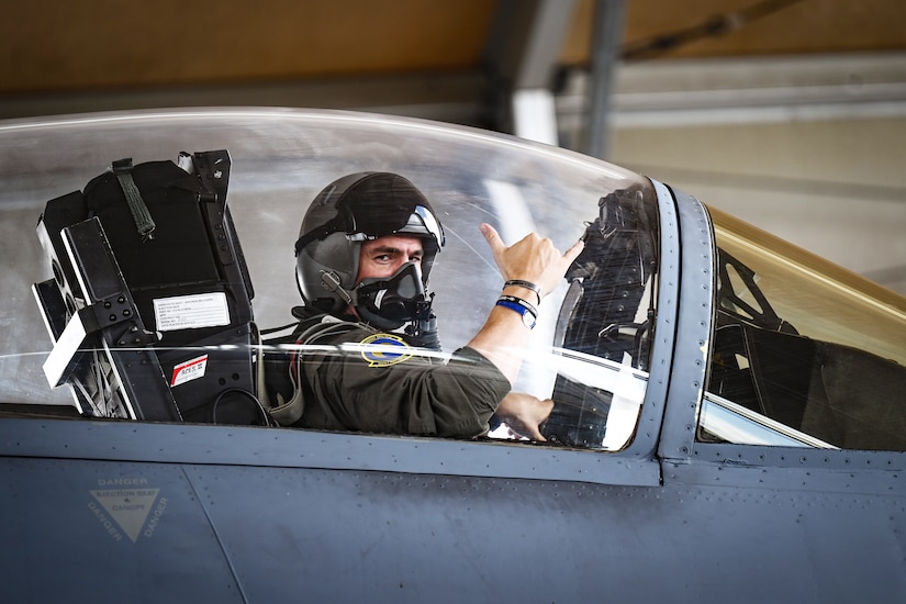 A pilot in an aircraft's cockpit gives a thumbs up sign.