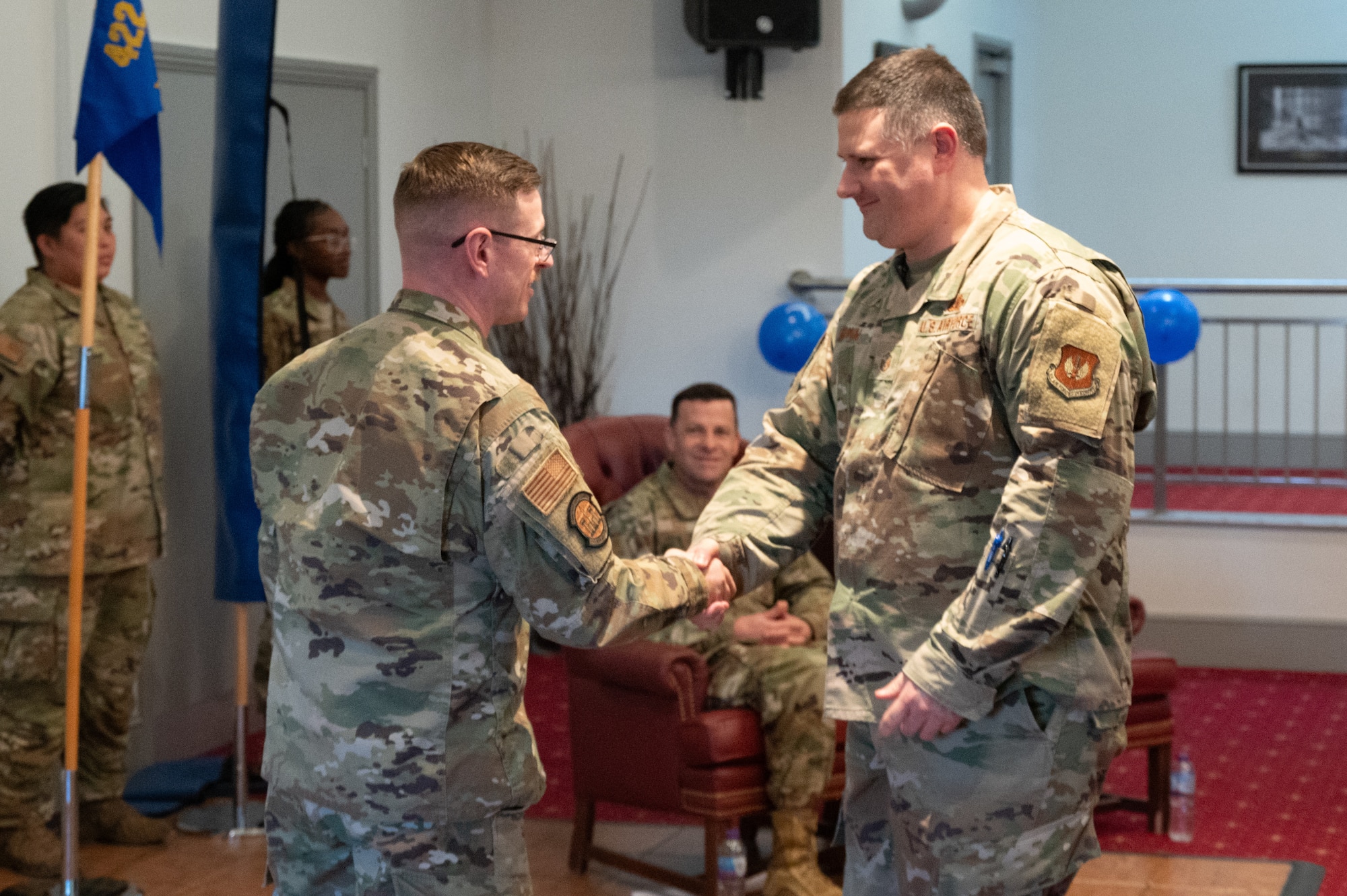 Airmen shake hands while passing a coin for excellence
