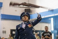 Photo of a U.S. Air Force honor guardsman throwing a ceremonial rifle overhead during a performance. A peer in the background observes.