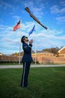 Photo of a U.S. Air Force honor guardsman tossing a rifle outside. The U.S. and Air Force flags wave in the background.
