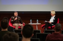 A uniformed military officer sitting on the stage, speaking to an audience of college students.