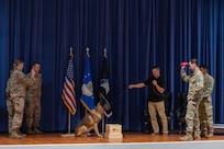 Military members toss toys to a military working dog on stage during his retirement ceremony.