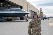 An Air National Guard crew chief gives a thumbs up signal to a B-2 Spirit stealth bomber emerging from a hangar on the Whiteman Air Force Base flight line. The Airman is wearing an OCP pattern uniform.