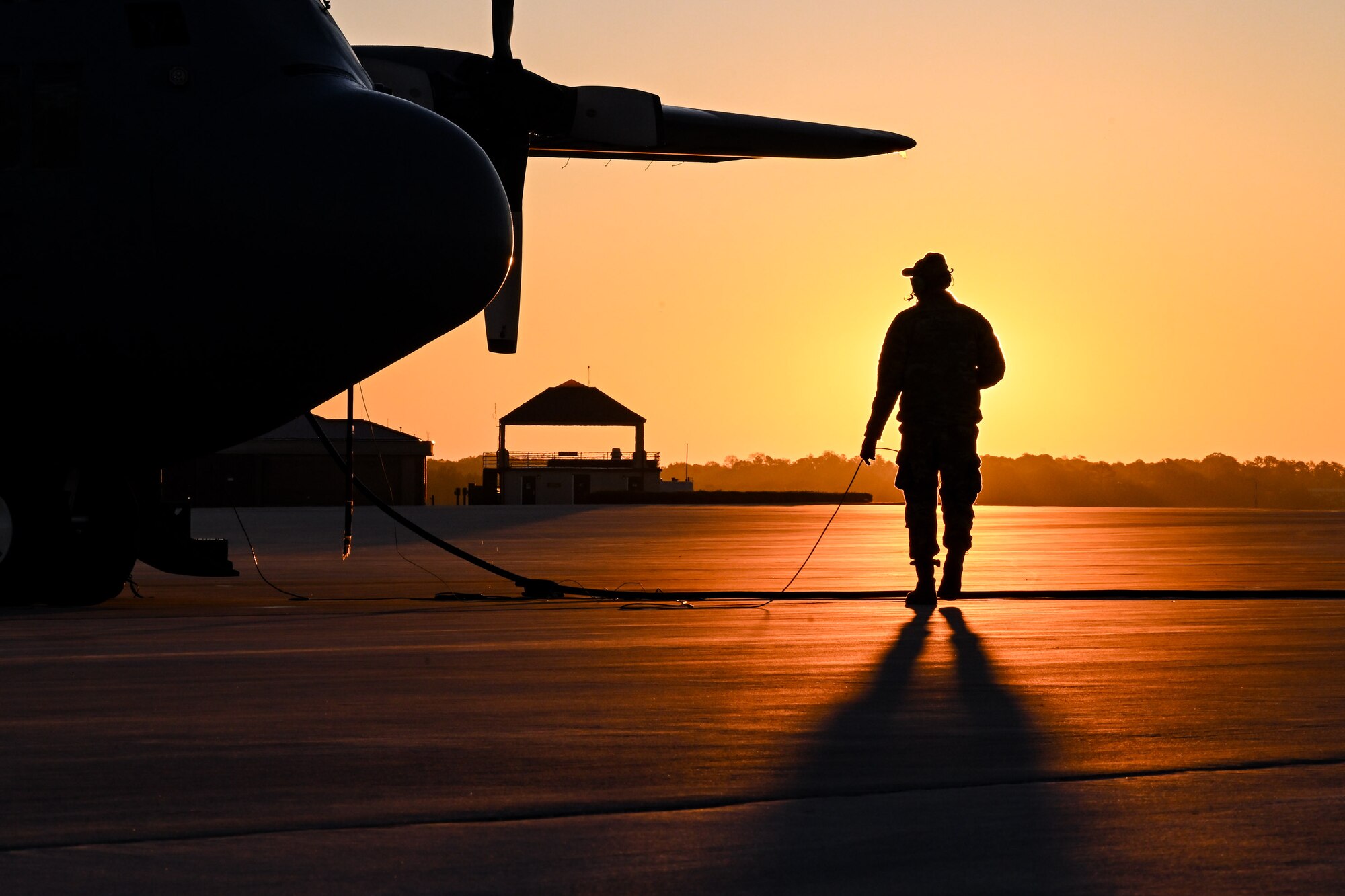 The sun rises behind a Citizen Airman assigned to the 910th Maintenance Squadron on the flightline at Dobbins Air Reserve Base, Georgia, Nov. 16, 2024.