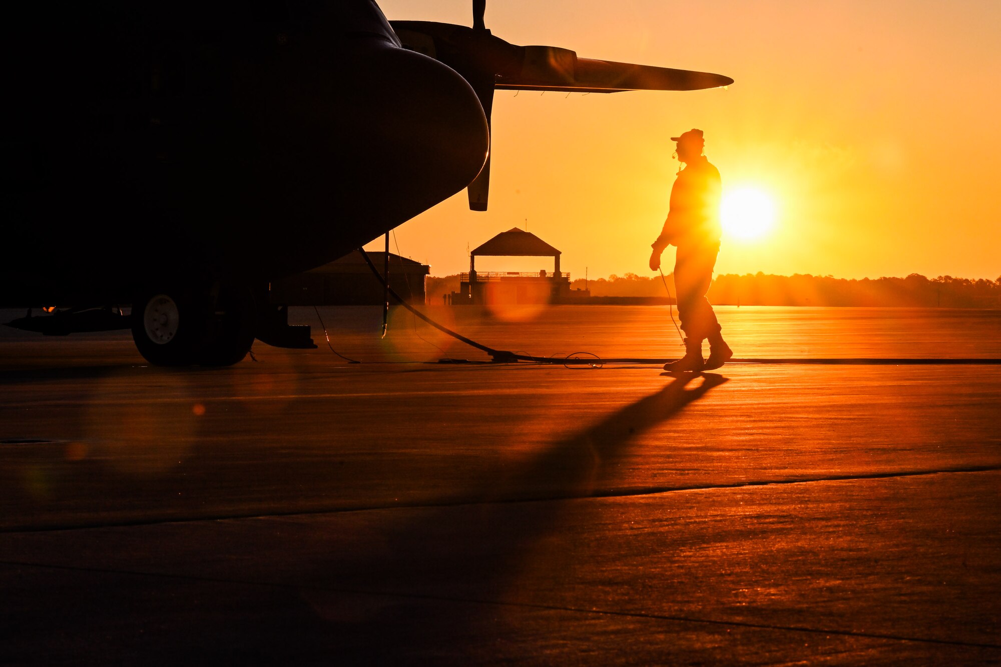 The sun rises behind a Citizen Airman assigned to the 910th Maintenance Squadron on the flightline at Dobbins Air Reserve Base, Georgia, Nov. 16, 2024.