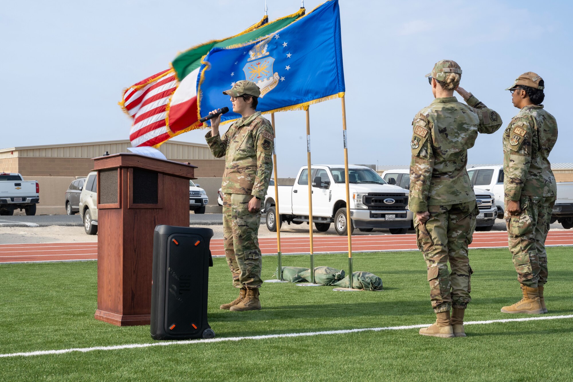 A U.S. Air Force Airman sings the national anthem during a ceremony while two other Airmen salute.