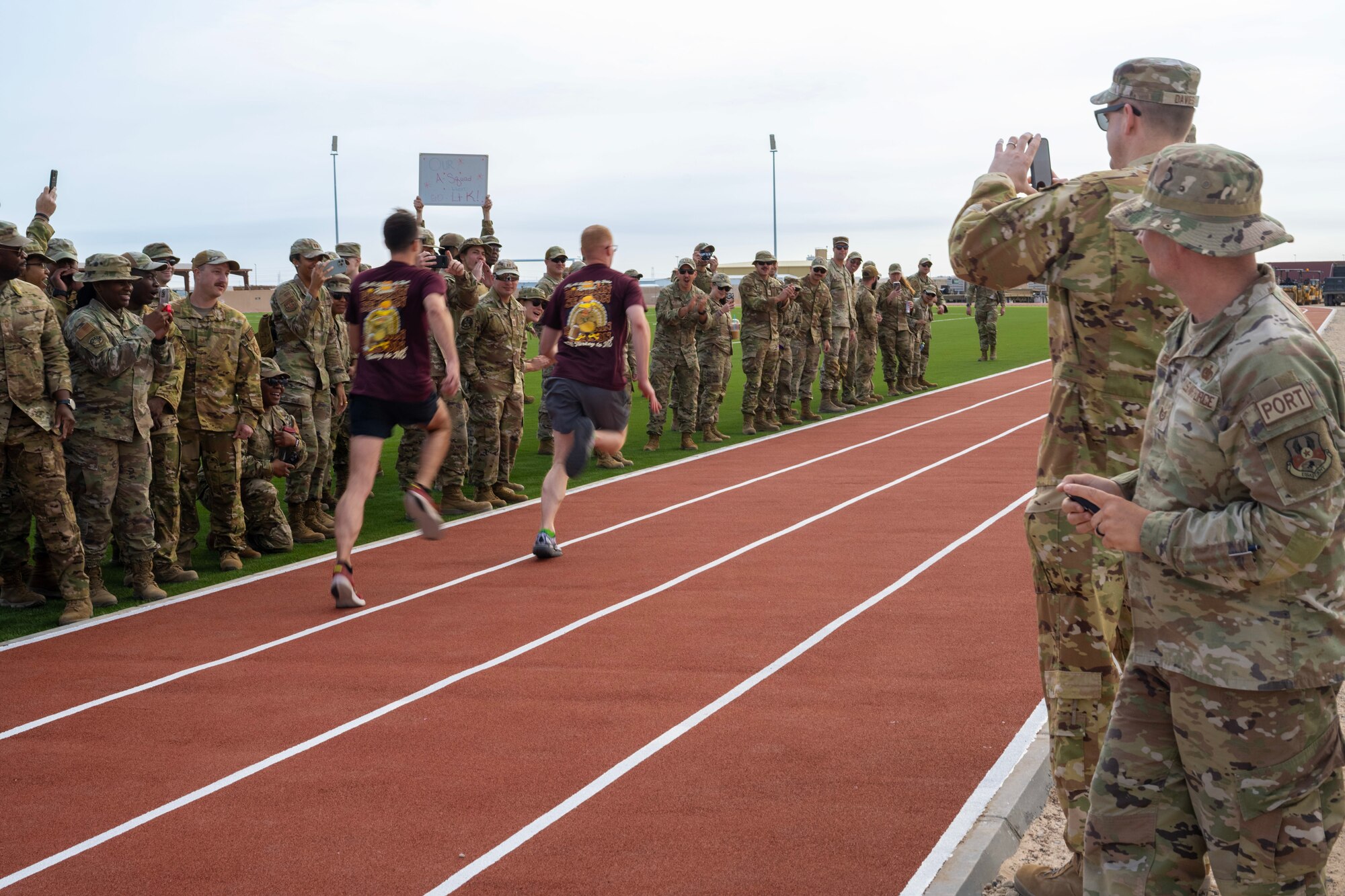 Two Airmen in civilian clothes begin a race to open a new track while military members in uniform cheer them on.