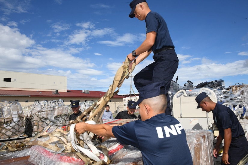 Volunteers in matching uniforms handle packaged cargo outdoors.