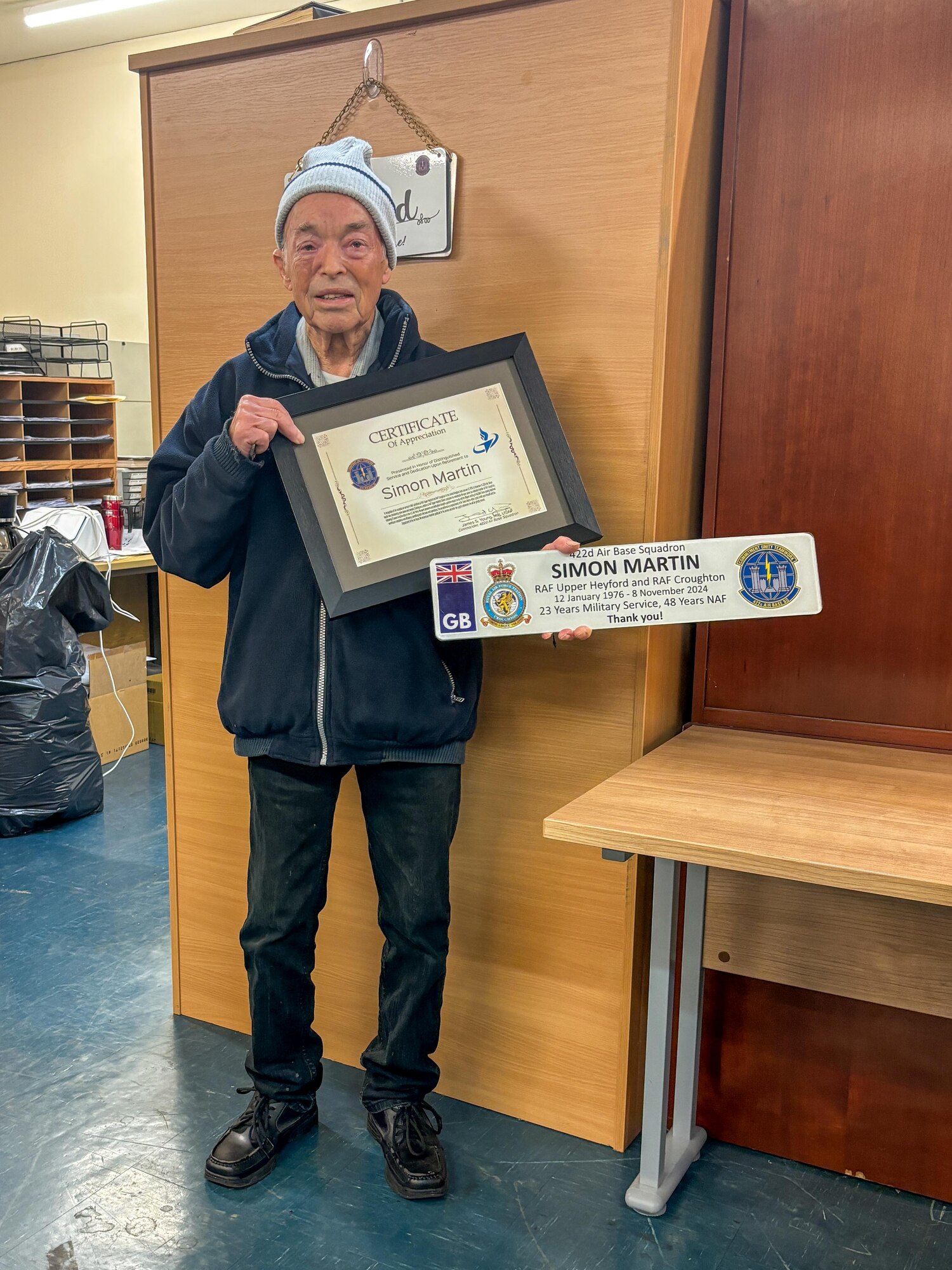 Mr. Simon Martin poses for a photo while holding two retirement mementos