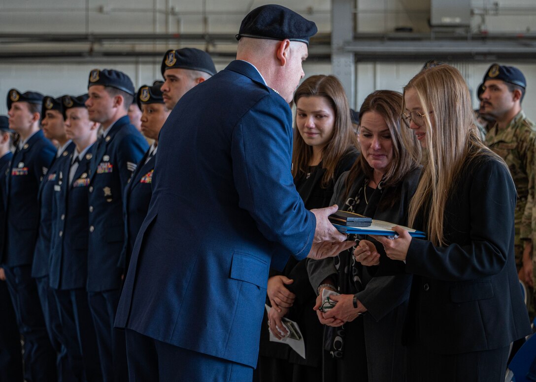 The spouse of Staff Sgt. Bailey Behzadi accepts two service awards on Behzadi’s behalf from U.S. Air Force Lt. Col. Timothy Marriner, 316th Security Forces Squadron commander, during a memorial service at Joint Base Andrews, Md., Oct. 21, 2024. In addition to Behazadi’s work in the 316th SFS, he served in the base honor guard and presented military honors at more than 90 veterans’ funerals across the east coast. (U.S. Air Force photo by Staff Sgt. Aubree Owens)