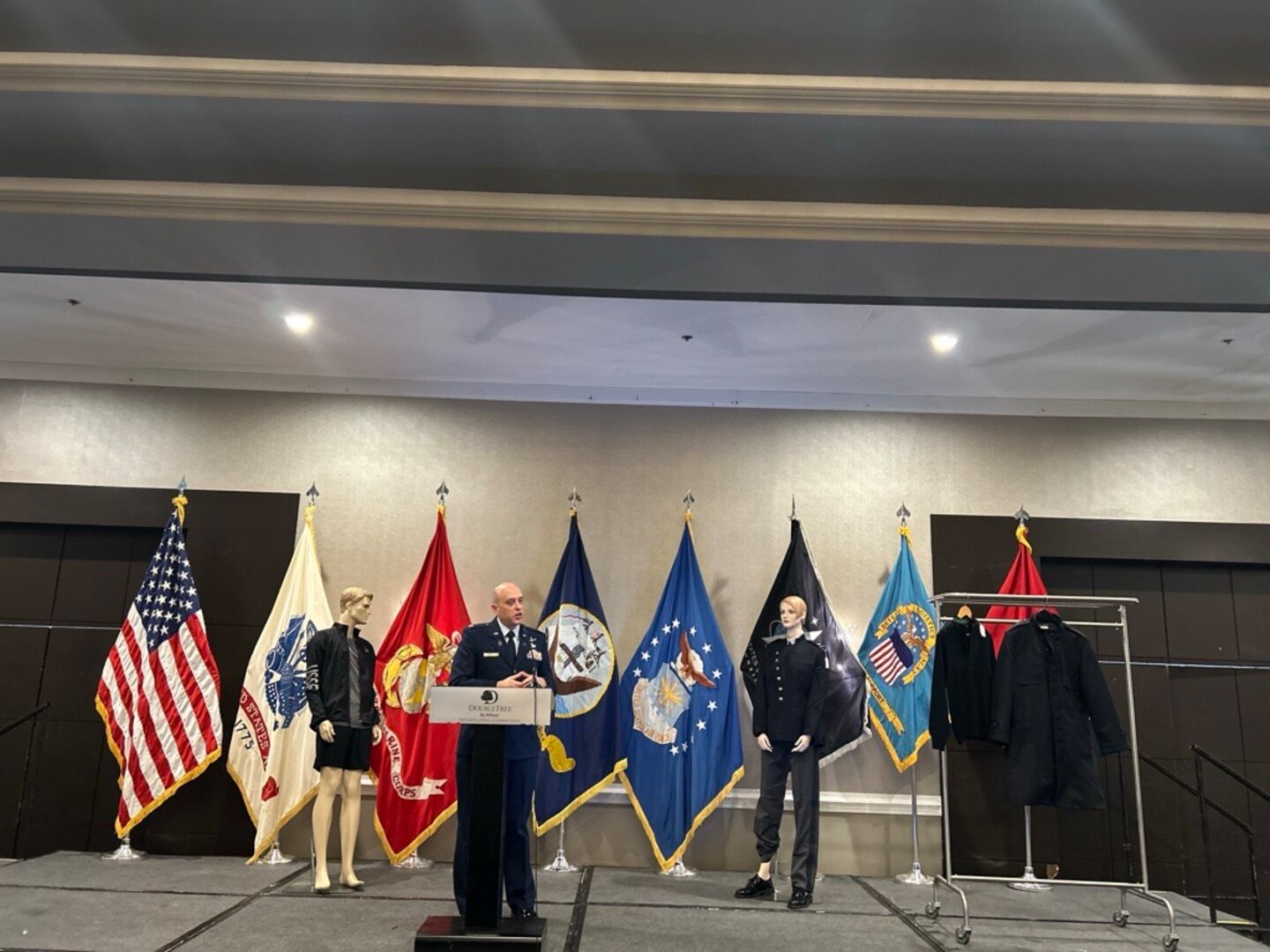 man in uniform stands on stage with mannequins in military dress uniforms