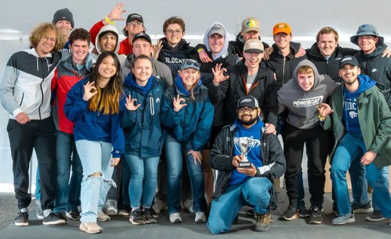 Several people stand in a group and pose for a picture with a small silver trophy in the front.