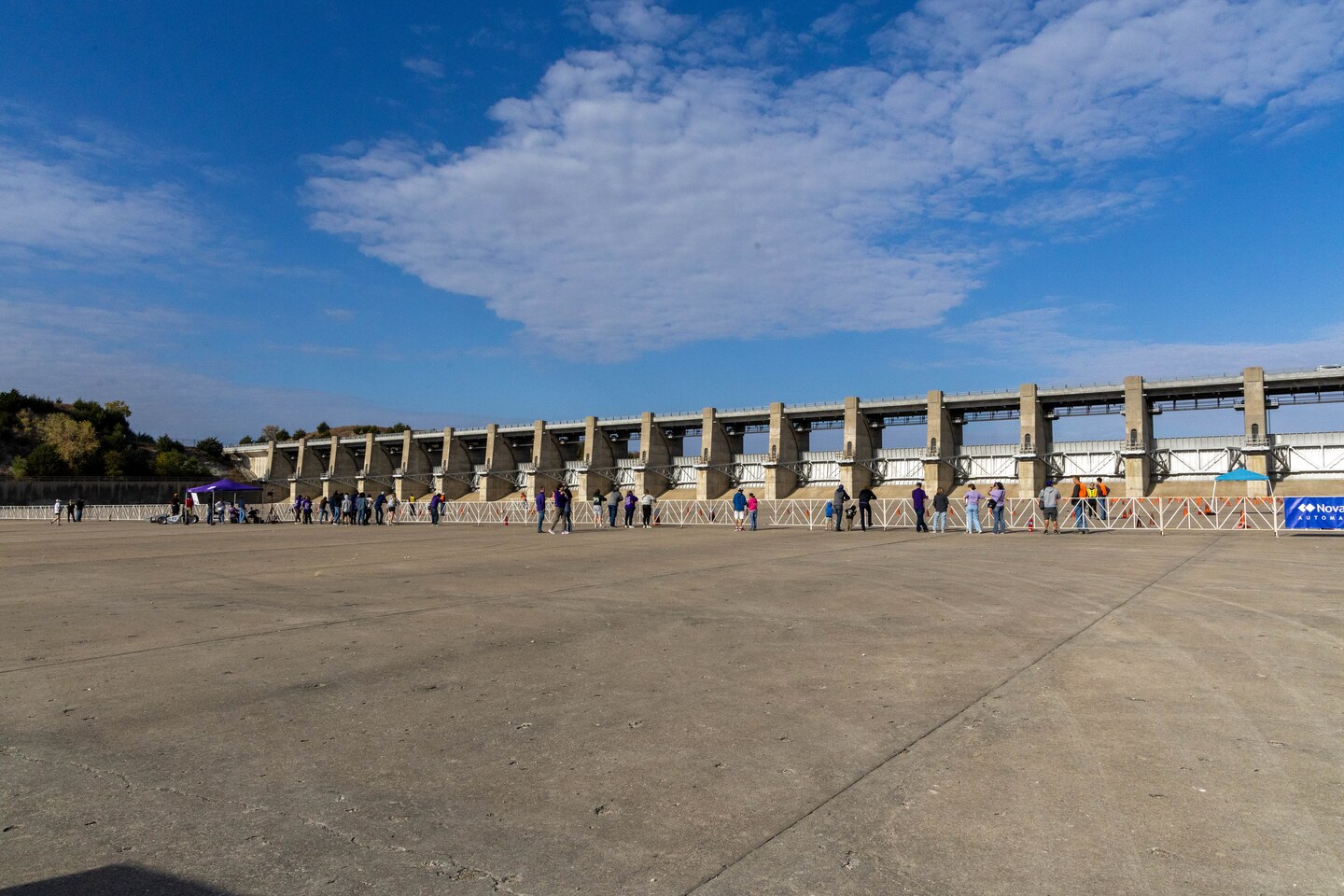 People stand in front of a white gate with grey concrete in the foreground and blue sky in the background.