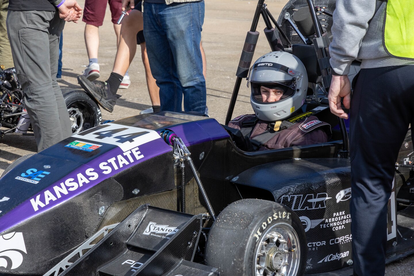 A purple and black formula one race car with a driver wearing a grey helmet.