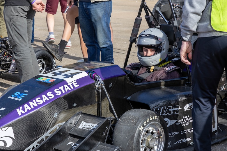 A purple and black formula one race car with a driver wearing a grey helmet.