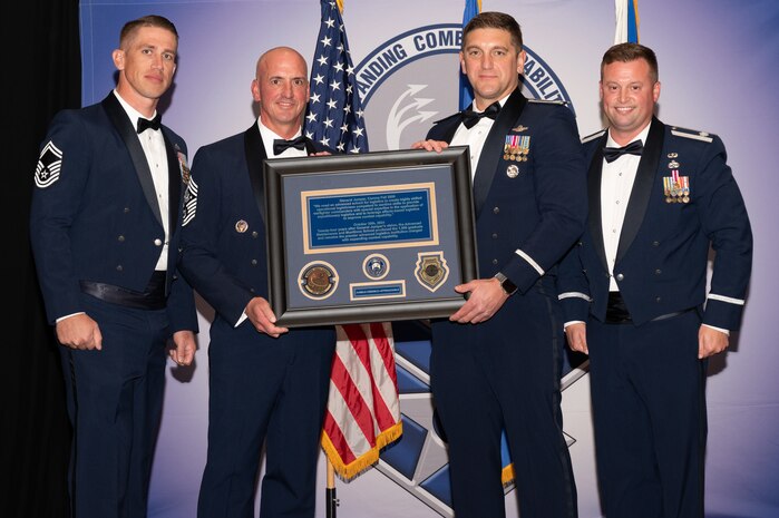Four people posing with plaque