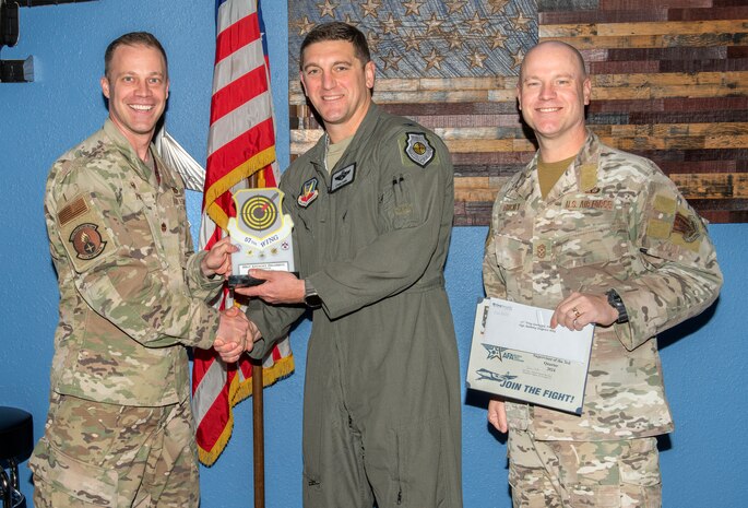 U.S. Air Force Chief Master Sgt. Jason K. Trickey, right, 57th Wing command chief, and Col. Ethan Sabin, center, 57th Wing deputy commander, present the Supervisor of the Quarter award to Maj. Talon M. Pope, commander of the 57th Munitions Squadron on behalf of Staff Sgt. Anthony Delgreco, a munitions support equipment maintenance crew chief scheduler assigned to the 57th Maintenance Group at Nellis Air Force Base, Nevada, Nov. 20, 2024.
