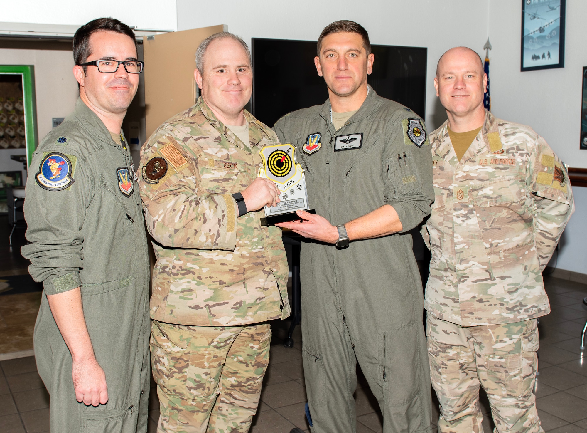 From right, U.S. Air Force Chief Master Sgt. Jason K. Trickey, 57th Wing command chief, and Col. Ethan E. Sabin, 57th Wing commander, present Master Sgt. Chase Beck, a flight chief assigned to the 66th Weapons School, with the Senior Noncommissioned Officer of the Quarter award at Nellis Air Force Base, Nevada, Nov. 20, 2024.