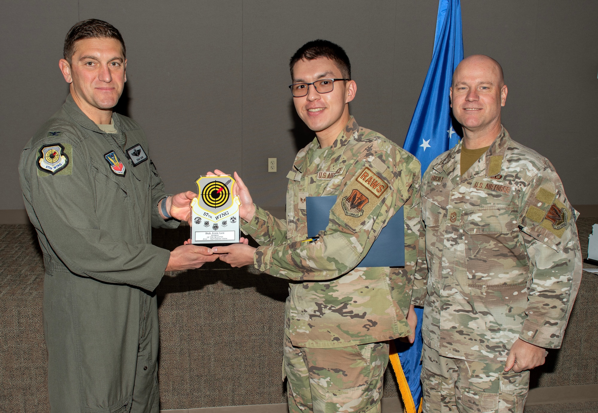 U.S. Air Force Col. Ethan E. Sabin, left, 57th Wing deputy commander, and Chief Master Sgt. Jason K. Trickey, right, 57th Wing command chief, present Senior Airman John Lee, a Radar, Airfield and Weather Systems technician assigned to the 57th Operational Support Squadron, with the Airman of the Quarter award at Nellis Air Force Base, Nevada, Nov. 20, 2024.