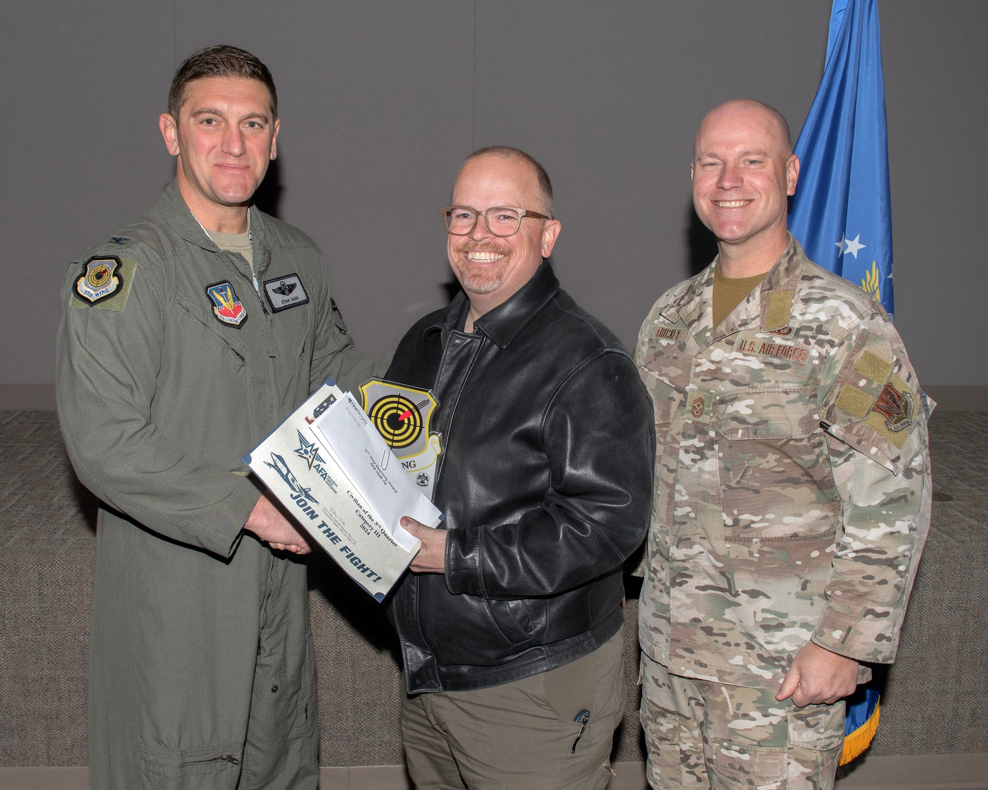 U.S. Air Force Col. Ethan Sabin, left, 57th Wing deputy commander, and Chief Master Sgt. Jason K. Trickey, right, 57th Wing command chief, present Jack Slade, an adversary network technician lead assigned to the 57th Information Aggressor Squadron, with the Civilian Category III of the Quarter award at Nellis Air Force Base, Nevada, Nov. 20, 2024.