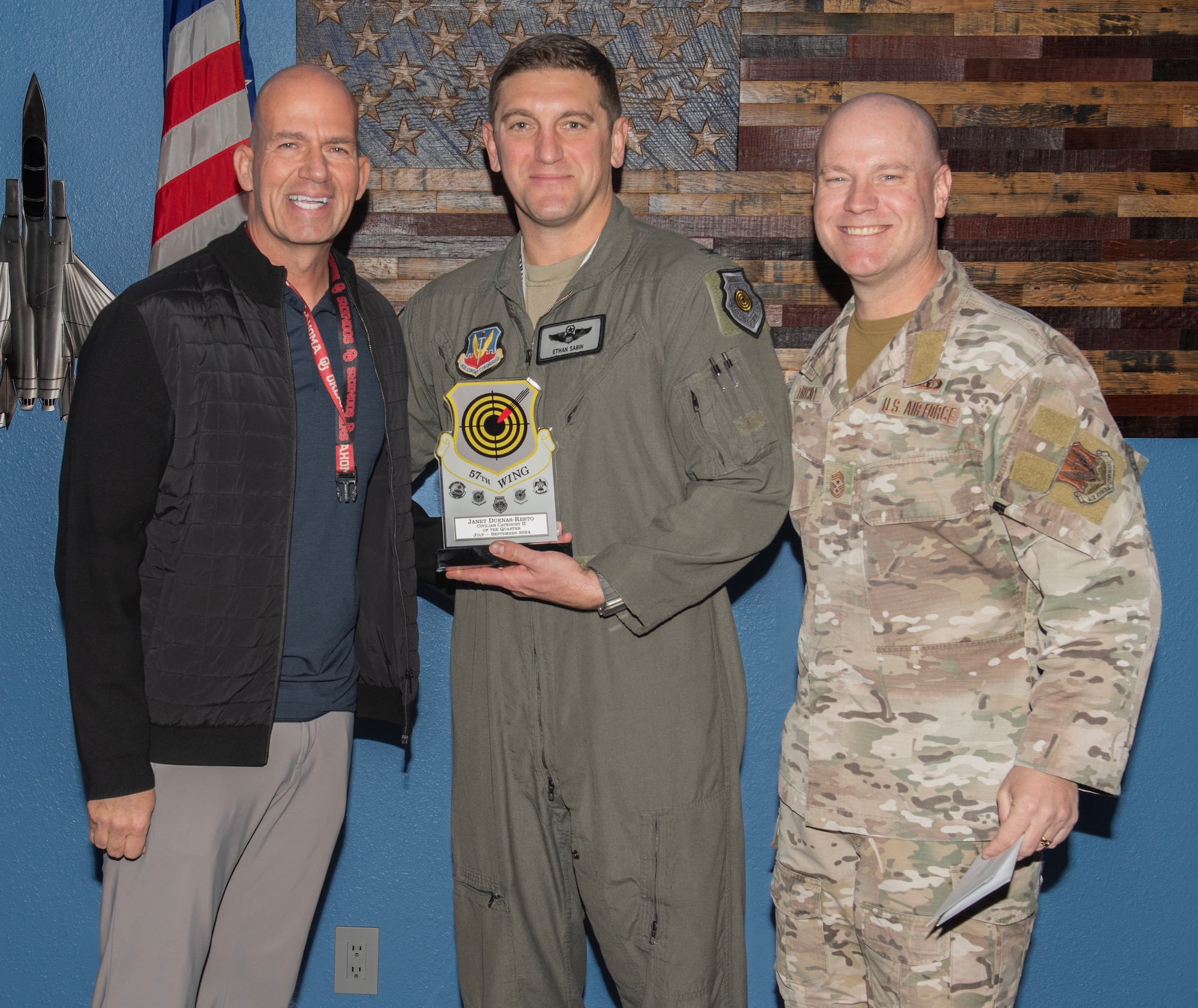 U.S. Air Force Col. Ethan Sabin, center, 57th Wing deputy commander, and Chief Master Sgt. Jason K. Trickey, right, 57th Wing command chief, present the Civilian Category II of the Quarter award on behalf of Janet Duenas-Resto, an executive services specialist with the 57th Maintenance Group at Nellis Air Force Base, Nevada, Nov. 20, 2024.