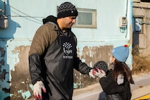 U.S. Army Staff Sgt. Miguel Bermejo, assigned to U.S. Army Garrison Yongsan-Casey Headquarters and Headquarters Company, gives a coal briquette to a child in the neighborhood of Sangpae, Dongducheon city, South Korea, Nov. 23, 2024.