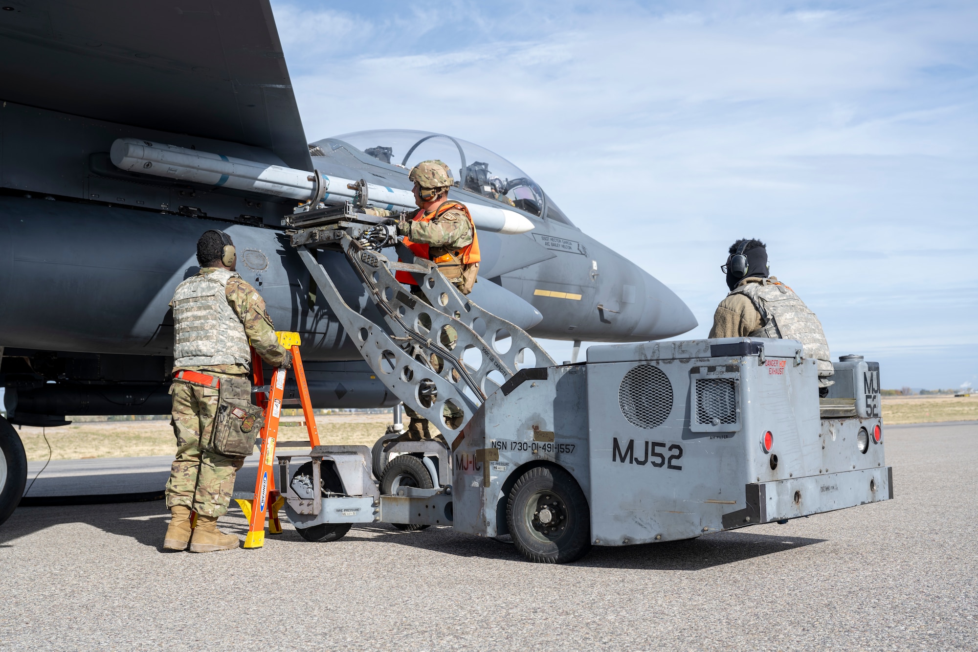 Three people load a practice bomb onto a jet
