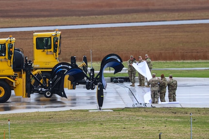 Two Alpena Combat Readiness Training Center snowplows cut the ribbon at the runway repair ceremony Nov. 25, 2024, in Alpena, Michigan. The two-year, $60 million federally funded construction project repaired the entire primary runway at Alpena County Regional Airport that supports military and commercial aircraft operations.