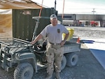 A man poses in front of an ATV in a desert location with tents.