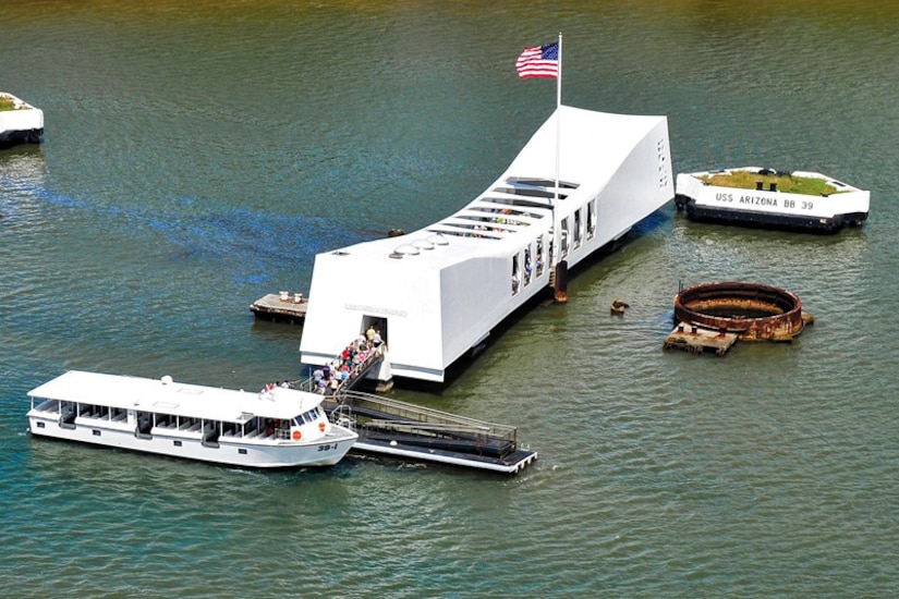 People disembark from a boat and walk into a white memorial structure that sits over water.