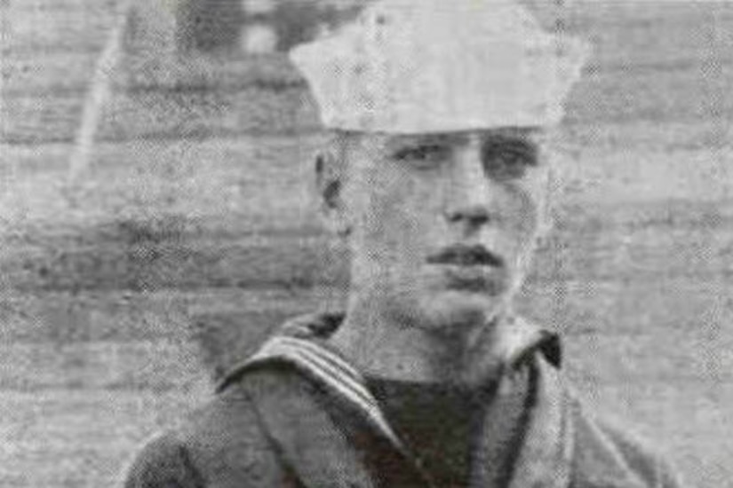 A sailor in uniform poses for a photo.