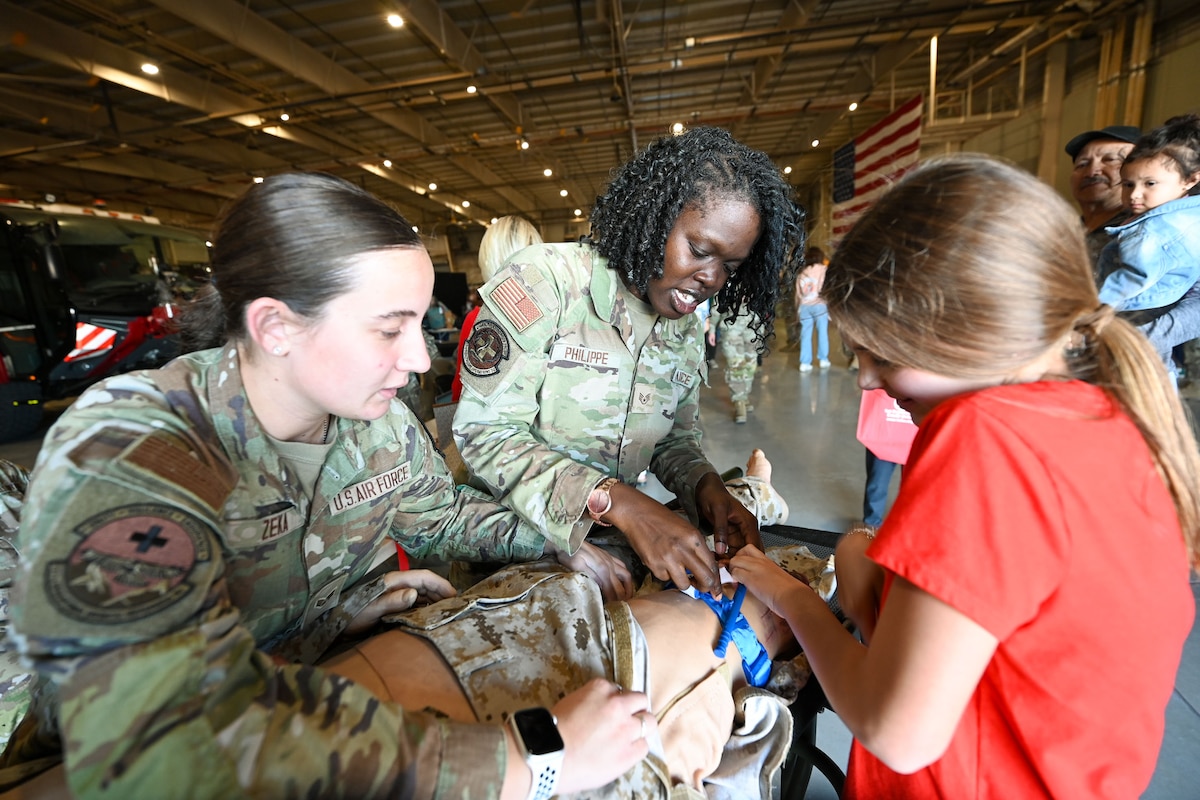 U.S. Air Force Senior Airman Vanesa Zeka, 17th Operational Medical Readiness Squadron flight medicine technician, left, and Staff Sgt. Nadialine Philippe, right, 17th Healthcare Operations Squadron immunization noncommissioned officer in charge, demonstrate to young participants how to apply a tourniquet during the 42nd annual Santa’s Market and 2nd annual Base Open House at the Louis F. Garland Department of Defense Fire Academy, Goodfellow Air Force Base, Texas, Nov. 23, 2024. Santa’s Market invited the community on base to learn more about Goodfellow's mission. (U.S. Air Force photo Airman 1st Class Evelyn J. D’Errico)