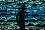 Silhouette of an individual in front of a digital screen displaying data. (Photo by Chris Yang on Unsplash.com)