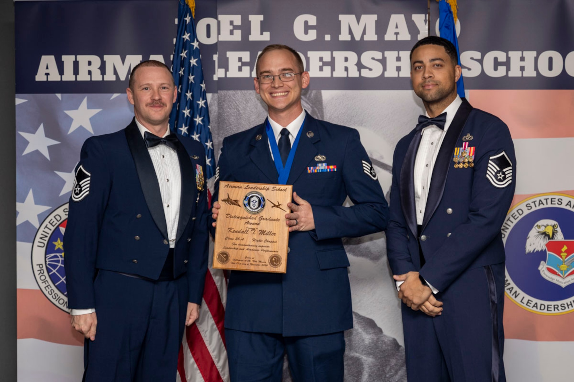 U.S. Air Force Staff Sgt. Kendall Miller, center, Airman Leadership Graduate, accepts the Distinguished Graduate Award from Master Sgt. Chaz Lineberger and Master Sgt. Nicholas Booker during the graduation of Joel C. Mayo ALS Class 25-A at Holloman Air Force Base, New Mexico, Nov. 21, 2024. The distinguished graduate award is presented to the top 10% of graduates for their performance in academic evaluations and demonstration of leadership. (U.S. Air Force photo by Airman 1st Class Michelle Ferrari)