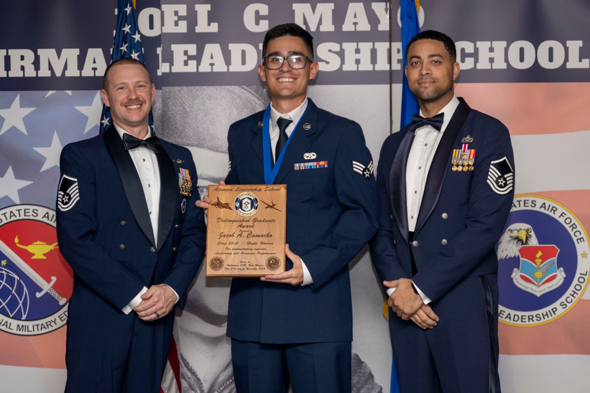 U.S. Air Force Senior Airman Jacob Camacho, center, Airman Leadership Graduate, accepts the Distinguished Graduate Award from Master Sgt. Chaz Lineberger and Master Sgt. Nicholas Booker during the graduation of Joel C. Mayo ALS Class 25-A at Holloman Air Force Base, New Mexico, Nov. 21, 2024. The distinguished graduate award is presented to the top 10% of graduates for their performance in academic evaluations and demonstration of leadership. (U.S. Air Force photo by Airman 1st Class Michelle Ferrari)