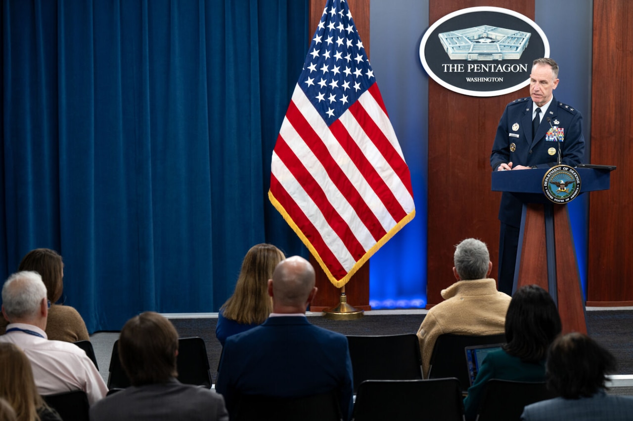 A man in a military uniform stands behind a lectern talking to an audience. The sign behind the lectern indicates that they are at the Pentagon.